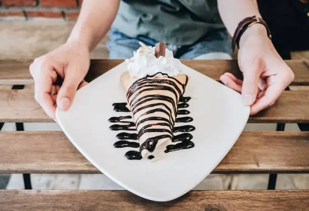 Photo of Cropped shot view of woman hands holding a plate of sweet chocolate cold crepe.