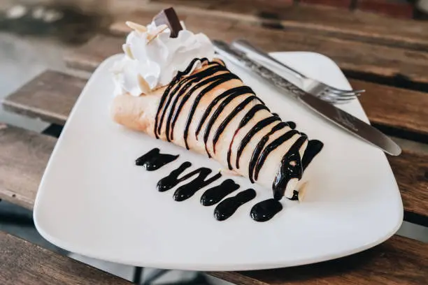 Photo of Close-up of sweet chocolate cold crepe on the wooden table.
