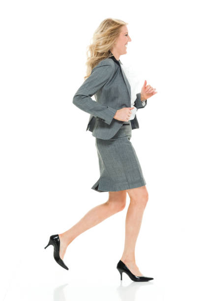 full length / side view / profile view of 20-29 years old adult beautiful blond hair caucasian young women / female business person / businesswoman / manager running / jogging / exercising in front of white background wearing skirt / a suit - 20 25 years profile female young adult imagens e fotografias de stock