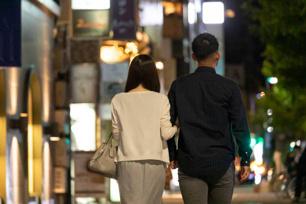 vista posteriore di uomo e donna che camminano tenendosi per mano in centro di notte - walking at night foto e immagini stock