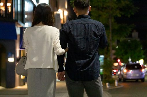 Back view of man and woman walking holding hands in downtown at night