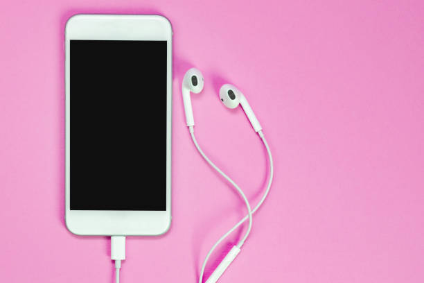 White smartphone on the pink background with headphones. View from above