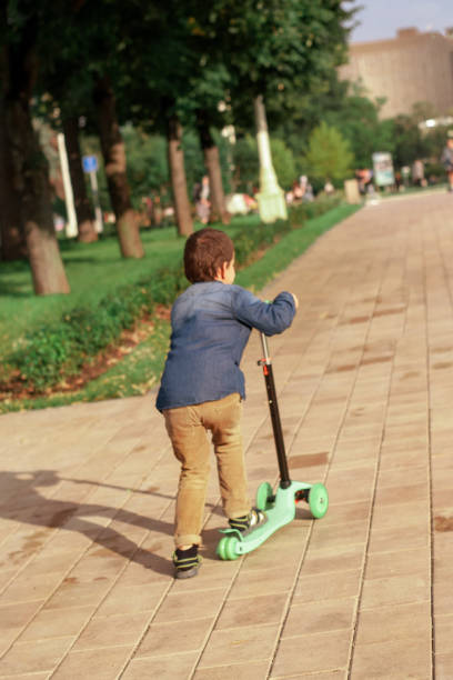 un garçon d'âge préscolaire apprend à monter un scooter dans un parc. les premiers pas dans le sport. sport avec intérêt. le sport est comme un jeu. - baby first steps autumn child photos et images de collection