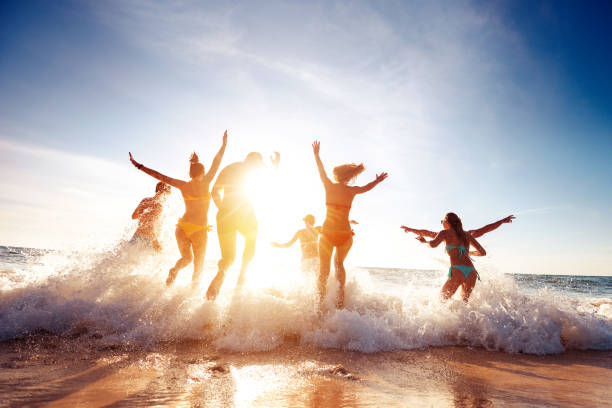 ビッググループの幸せな友人が実行し、夕日のビーチで楽しみを持っています - beach ストックフォトと画像