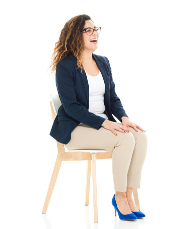 Full length / side view / profile view of 30-39 years old adult beautiful curly hair / long hair latin american and hispanic ethnicity / puerto rican ethnicity female / young women businesswoman / business person sitting / resting in front of white background wearing eyeglasses / t-shirt / shirt / blazer - jacket / jacket / pants and high heels who is smiling / happy / cheerful / sitting on chair