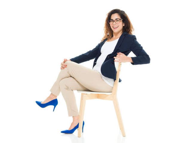 Full length / side view / profile view / looking at camera of 30-39 years old adult beautiful curly hair / long hair latin american and hispanic ethnicity / puerto rican ethnicity female / young women businesswoman / business person sitting / resting in front of white background wearing eyeglasses / t-shirt / shirt / blazer - jacket / jacket / pants and high heels who is smiling / happy / cheerful / sitting on chair longitud completa / vista lateral / vista de perfil / mirando a la cámara de 30-39 años adulto hermoso pelo rizado / pelo largo latino y etnia hispana / etnia puertorican femenina / joven mujer de negocios / persona de negocios sentado / descansando