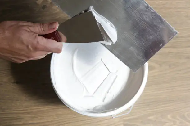 Man plastering wall with putty-knife, close up image. Fixing wall surface and preparation for painting.