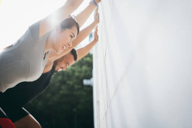 confiança e pares desportivos novos energéticos que fazem esticando o exercício sobre a parede ao ar livre no parque da cidade na manhã - couple stretching running jogging - fotografias e filmes do acervo