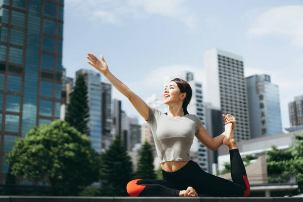 athletische junge asiatische frau üben yoga im freien im stadtpark gegen stadtbild am morgen - warming up fotos stock-fotos und bilder
