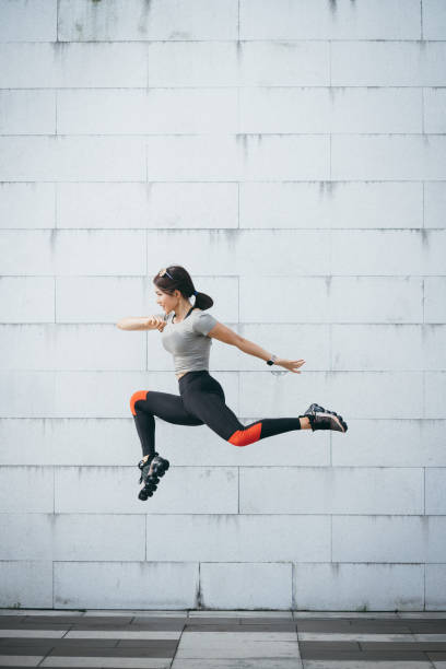 pewność siebie i energiczna młoda sportowa kobieta skacząca w powietrzu o szarą ścianę w parku miejskim - jumping women running vitality zdjęcia i obrazy z banku zdjęć