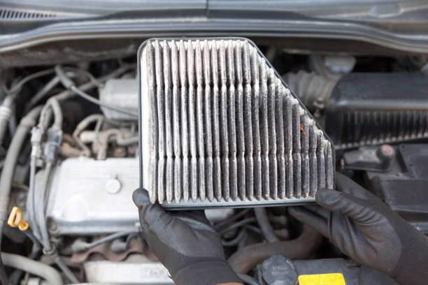 Auto mechanic wearing protective work gloves holding dirty used air filter above a car engine stock photo