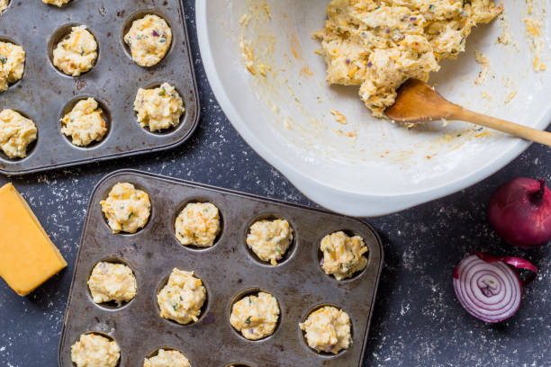 istock Cheddar cheese and herbs mini muffin dough uncooked being placed in muffin baking trays 1174091671