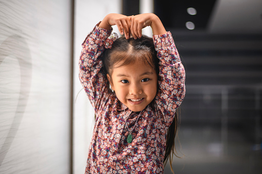 Cute four year old Chinese girl gesturing with her arms to make shape of heart while looking at camera.