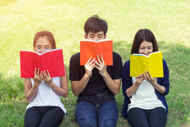 istock Group of students reading on green grass in park. Education concept. 1174101943