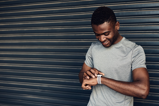Shot of a sporty young man checking his watch while exercising against a grey background