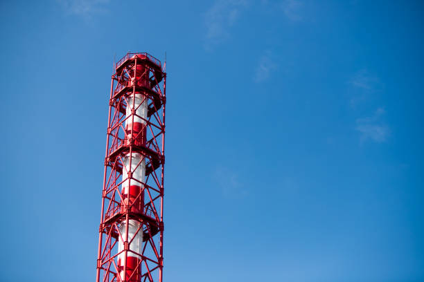 Red and white chemical plant pipe throws harmful poisonous smoke into clear blue sky with copy space. Concept of greenhouse effect and air pollution due to fuel combustion and chemical production.