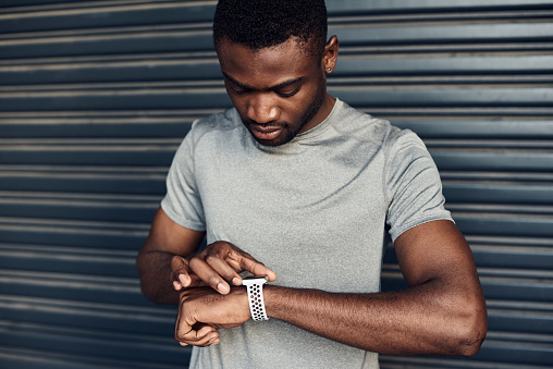 Shot of a sporty young man checking his watch while exercising against a grey background
