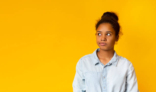 Annoyed african girl looking aside at free space Annoyed african teen looking aside at free space on yellow studio background. skeptical look stock pictures, royalty-free photos & images