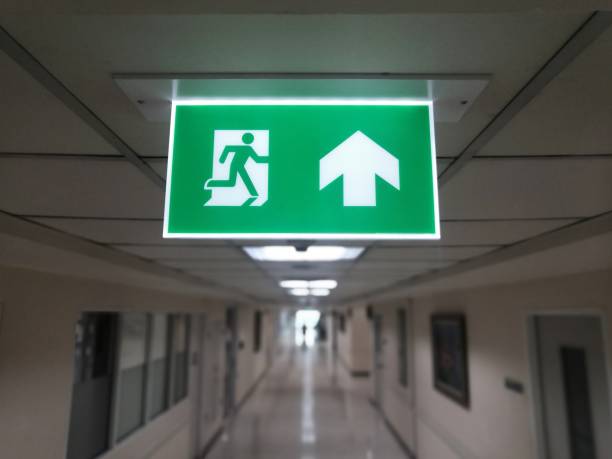 istock Emergency Fire exit sign hanging on top of the building in modern offices inside. Fire exit sign indicating safe route. 1174105909
