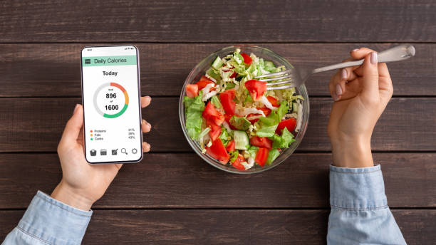 야채 샐러드를 먹고 모바일 응용 프로그램에 칼로리를 계산하는 여자 - 탄수화물 음식 뉴스 사진 이미지
