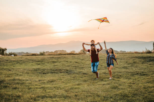 Family enjoying together Young caucasian parents and their daughter running on a meadow with kite. Father carrying daughter on his shoulders. simple living stock pictures, royalty-free photos & images