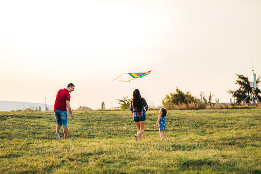 Young caucasian parents and their daughter running on a meadow with kite.