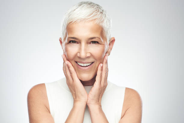 Senior woman posing in front of gray background. Beautiful smiling senior woman with short gray hair posing in front of gray background. Beauty photography. antiaging stock pictures, royalty-free photos & images