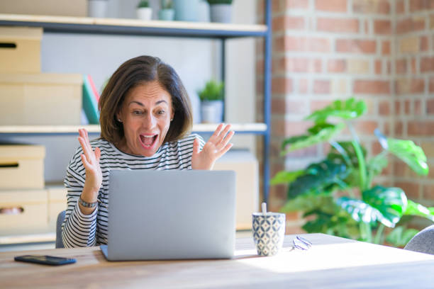 istock Middle age senior woman sitting at the table at home working using computer laptop very happy and excited, winner expression celebrating victory screaming with big smile and raised hands 1174112512