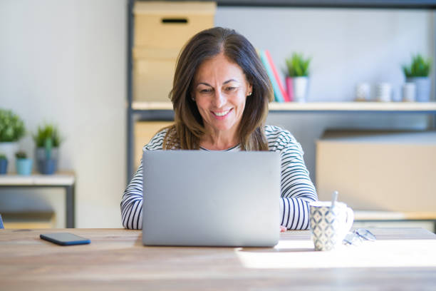 istock Middle age senior woman sitting at the table at home working using computer laptop with a happy and cool smile on face. Lucky person. 1174112615