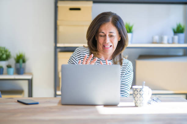 istock Middle age senior woman sitting at the table at home working using computer laptop disgusted expression, displeased and fearful doing disgust face because aversion reaction. With hands raised. Annoying concept. 1174112849