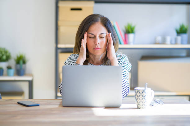 istock Middle age senior woman sitting at the table at home working using computer laptop with hand on head for pain in head because stress. Suffering migraine. 1174113720
