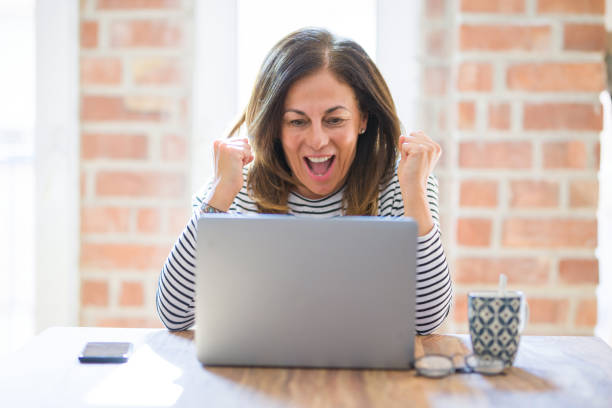 istock Middle age senior woman sitting at the table at home working using computer laptop screaming proud and celebrating victory and success very excited, cheering emotion 1174113971