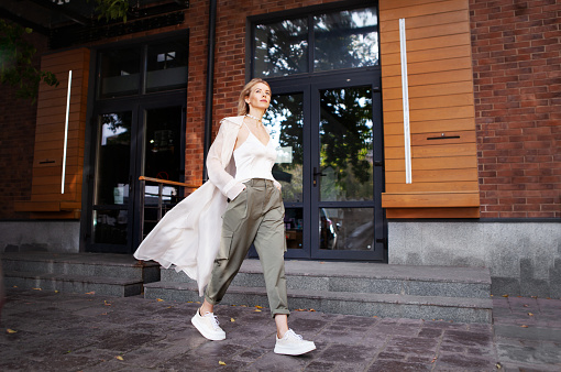 estilo de moda callejera. Hermosa mujer sexy que lleva ropa de primavera o otoño de moda (capa de trinchera beige, pantalones de carga, accesorio) al aire libre. Femenino elegante modelo caminando Street. Tendencia de otoño photo