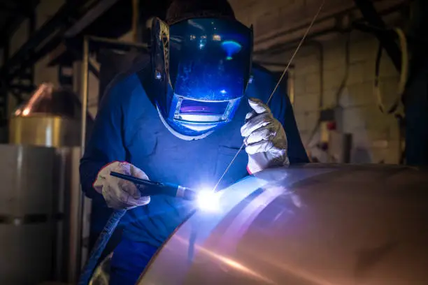 Welder welding stainless steel tank at industry workshop