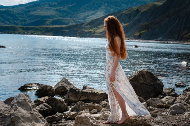 istock Beautiful boho styled model wearing white dress posing on the beach in sunlight 1174129162