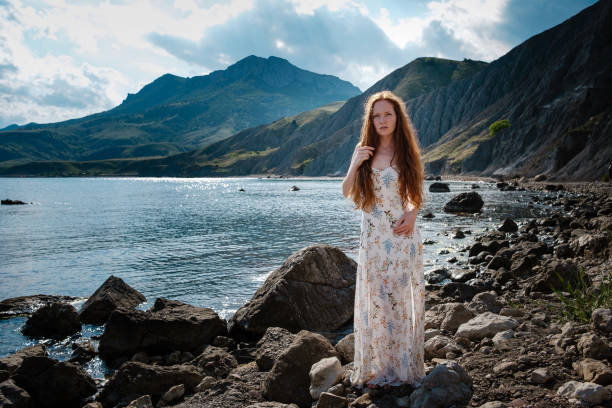 istock Beautiful boho styled model wearing white dress posing on the beach in sunlight 1174129370
