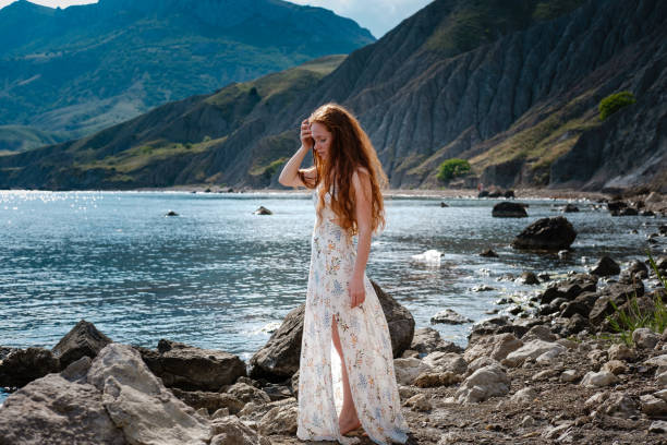 istock Beautiful boho styled model wearing white dress posing on the beach in sunlight 1174129535