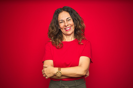 Middle age senior woman with curly hair over red isolated background happy face smiling with crossed arms looking at the camera. Positive person.