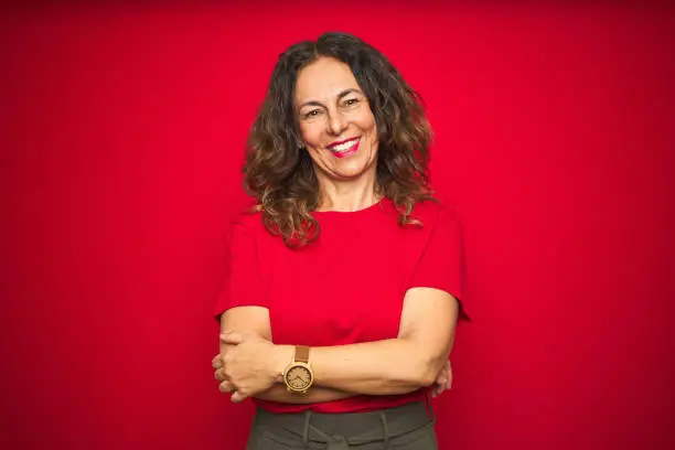 Photo of Middle age senior woman with curly hair over red isolated background happy face smiling with crossed arms looking at the camera. Positive person.