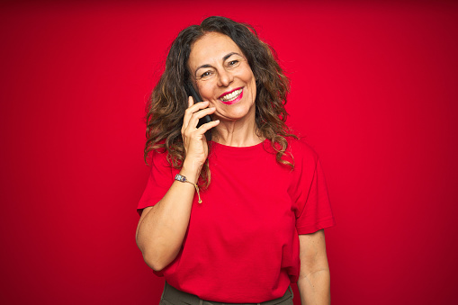 Middle age senior woman talking on the phone over red isolated background with a happy face standing and smiling with a confident smile showing teeth