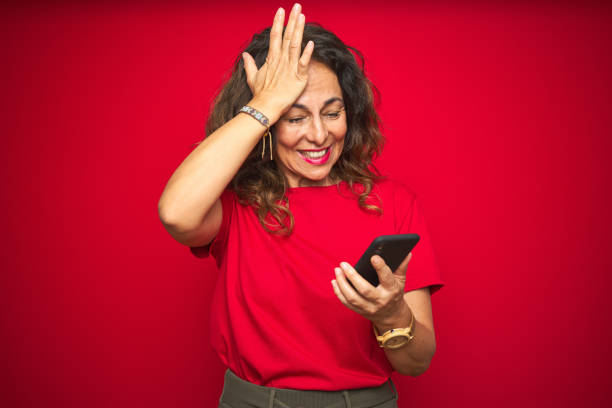 istock Middle age senior woman using smartphone over red isolated background stressed with hand on head, shocked with shame and surprise face, angry and frustrated. Fear and upset for mistake. 1174133376