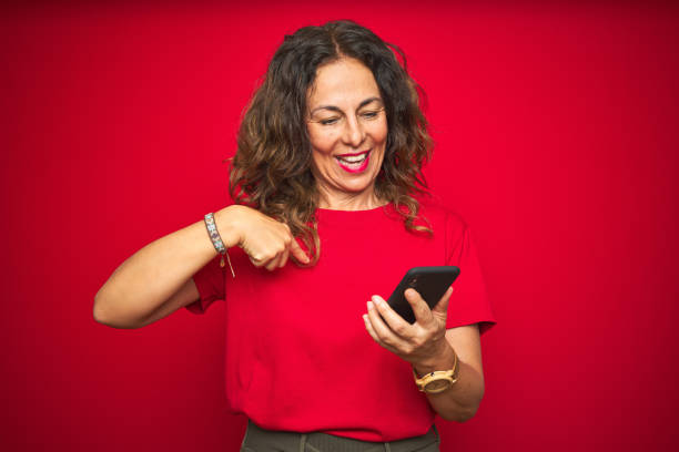 istock Middle age senior woman using smartphone over red isolated background with surprise face pointing finger to himself 1174133413