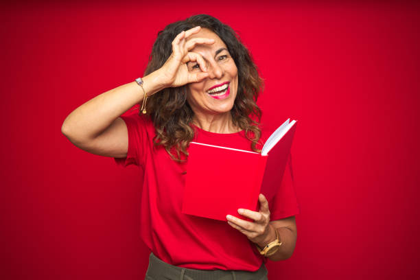 middle age senior woman reading a book over red isolated background with happy face smiling doing ok sign with hand on eye looking through fingers - women professor mature adult human face imagens e fotografias de stock