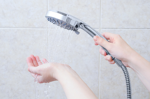 Caucasian girl holding a shower watering can. Jets of water on hand. Background beige tile.