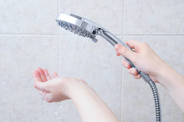 Caucasian girl holding a shower watering can. Jets of water on hand. Background beige tile. Caucasian girl holding a shower watering can. Jets of water on hand. Background beige tile. shower head stock pictures, royalty-free photos & images