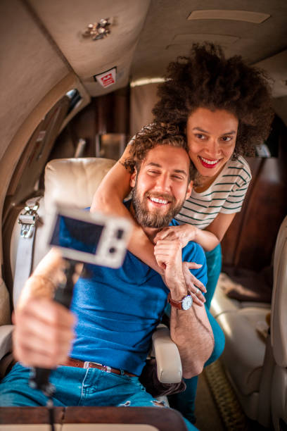 istock Young female afro-american vlogger shooting content while hugging her partner from behind on a private airplane 1174136419