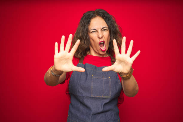 istock Middle age senior woman wearing apron uniform over red isolated background doing stop gesture with hands palms, angry and frustration expression 1174136845