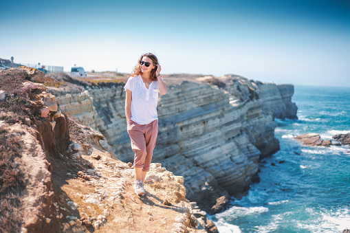 Beautiful young woman with a happy smile in a white T-shirt on the ocean in Portugal, travel and relax