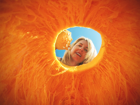 A woman looking inside of a jack o' lantern that she is carving from the perspective of inside the pumpkin.