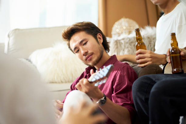 istock young asian man playing guitar during gathering 1174146440